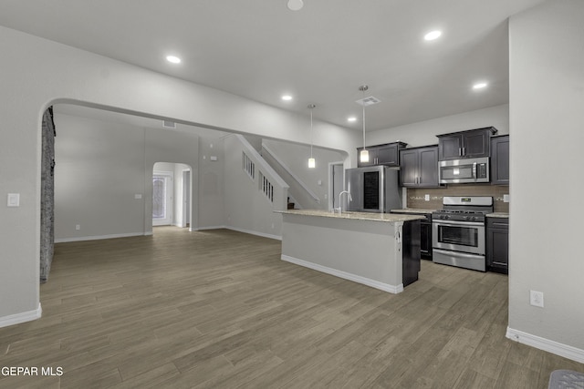 kitchen with open floor plan, appliances with stainless steel finishes, light wood-style floors, arched walkways, and a sink