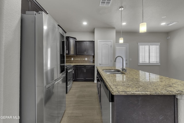 kitchen featuring visible vents, an island with sink, a sink, tasteful backsplash, and appliances with stainless steel finishes