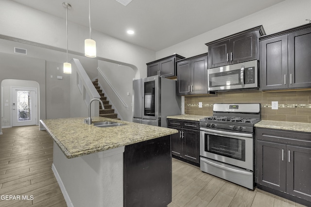 kitchen featuring visible vents, a sink, backsplash, stainless steel appliances, and arched walkways