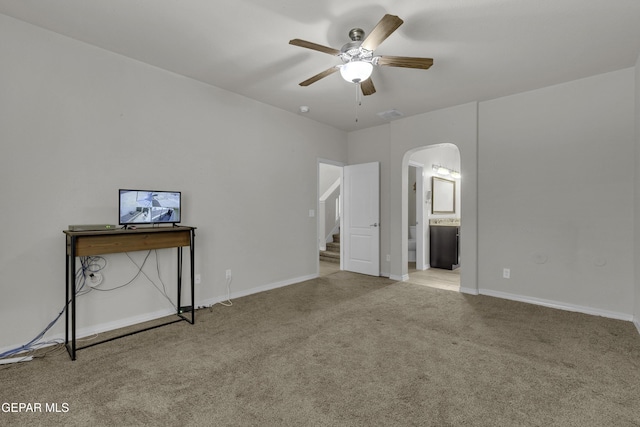 interior space with carpet, baseboards, arched walkways, ceiling fan, and connected bathroom