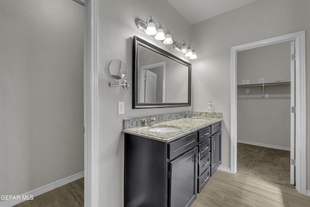 bathroom with double vanity, wood finished floors, baseboards, and a sink