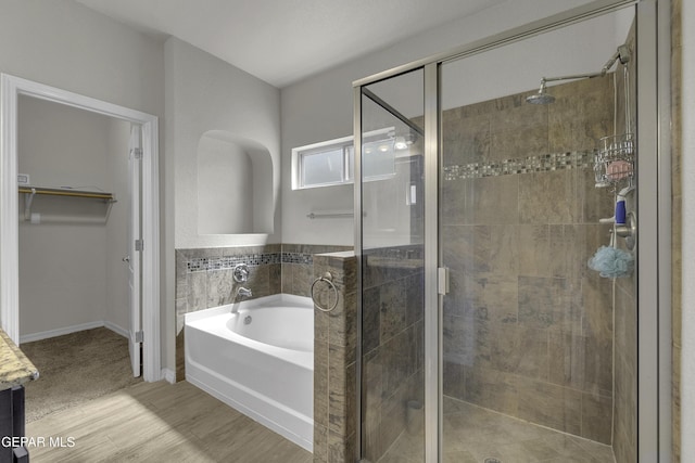 bathroom with a walk in closet, a garden tub, wood finished floors, and a shower stall