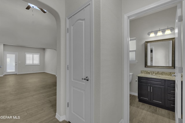 corridor with baseboards, light wood-style floors, arched walkways, and a sink