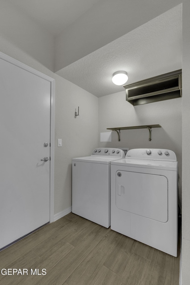 laundry room featuring baseboards, light wood finished floors, laundry area, a textured ceiling, and washing machine and dryer