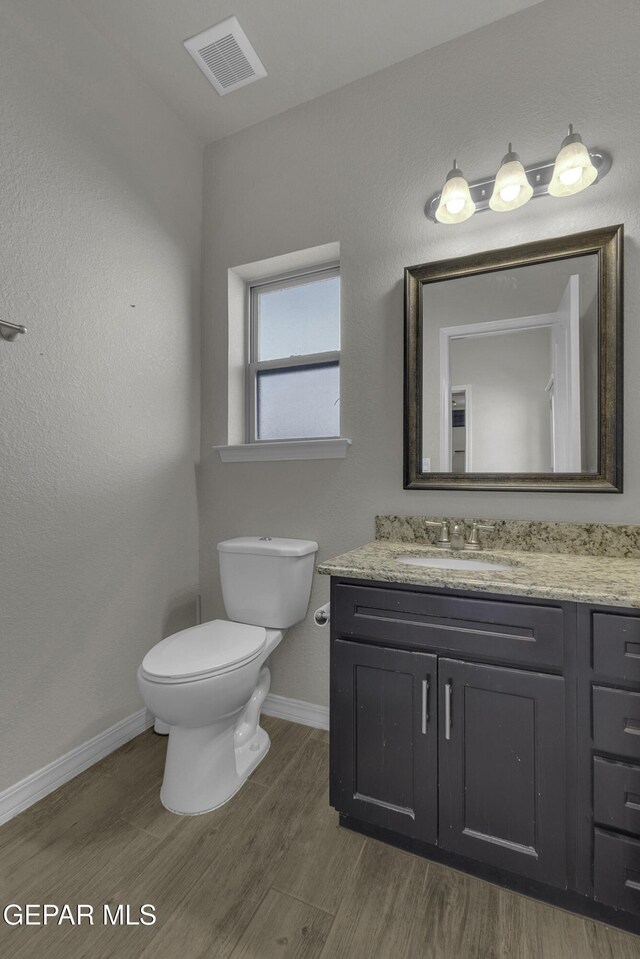 half bath with visible vents, baseboards, toilet, wood finished floors, and vanity