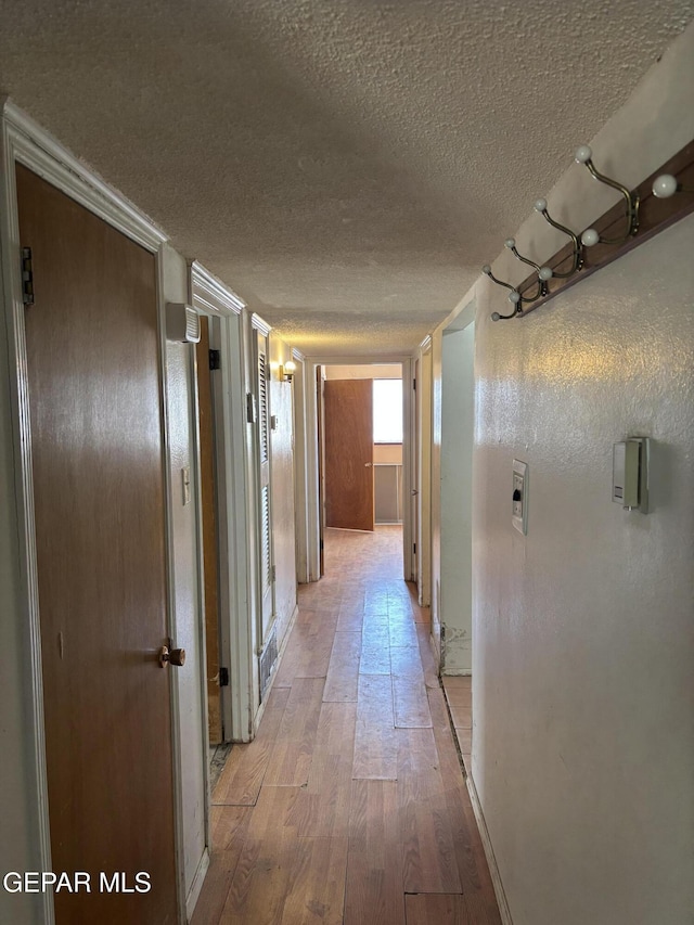 corridor featuring light wood-type flooring and a textured ceiling