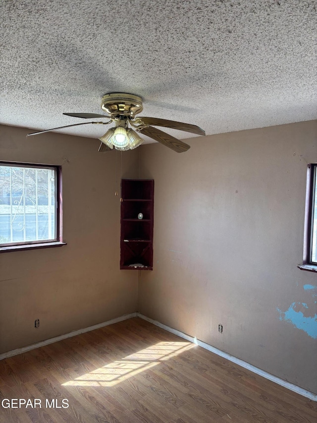 unfurnished room featuring a textured ceiling, a ceiling fan, baseboards, and wood finished floors