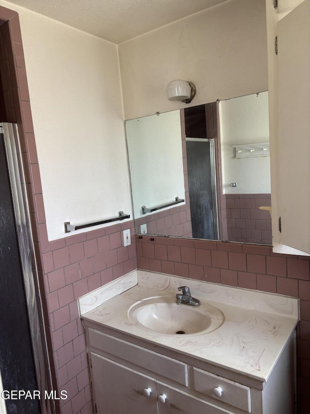 full bath featuring tile walls, a stall shower, and vanity