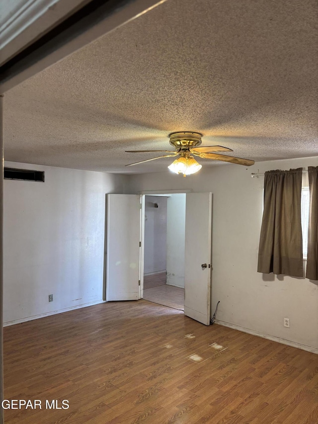 unfurnished room with ceiling fan, light wood-style flooring, and a textured ceiling