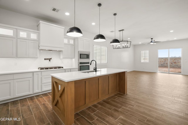 kitchen featuring premium range hood, wood tiled floor, stainless steel appliances, a sink, and light countertops