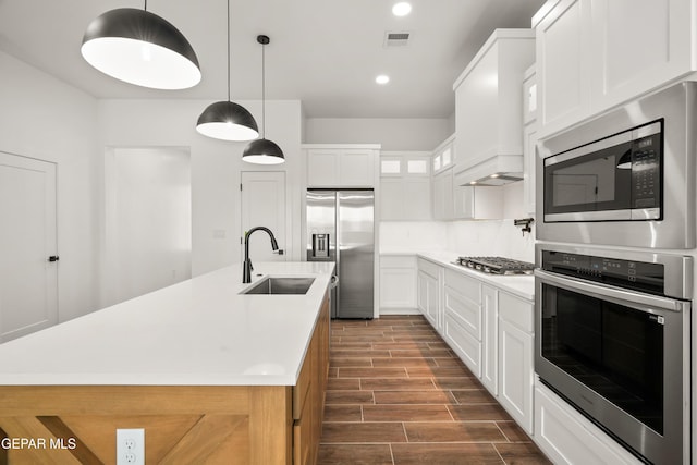 kitchen with wood finish floors, visible vents, custom range hood, a sink, and stainless steel appliances