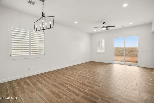 empty room featuring visible vents, ceiling fan with notable chandelier, dark wood finished floors, recessed lighting, and baseboards