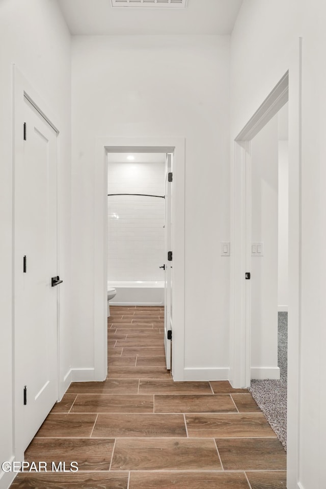 hallway featuring visible vents, baseboards, and wood tiled floor