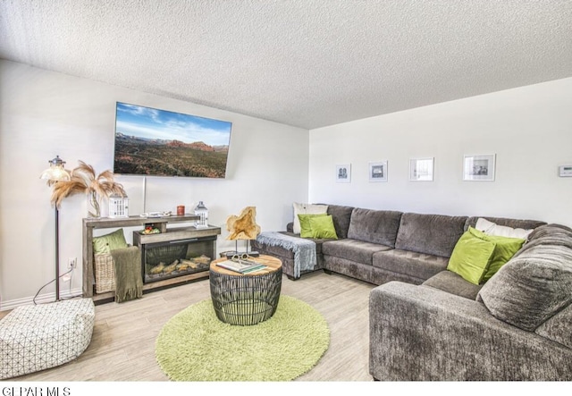 living area with a glass covered fireplace, a textured ceiling, baseboards, and wood finished floors