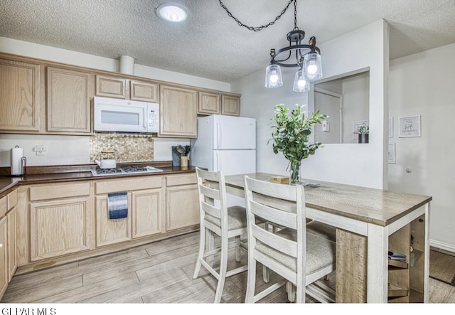 kitchen with dark countertops, white appliances, a textured ceiling, and light wood-style floors