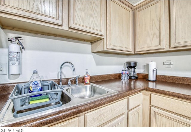 kitchen featuring dark countertops, cream cabinets, light brown cabinetry, and a sink