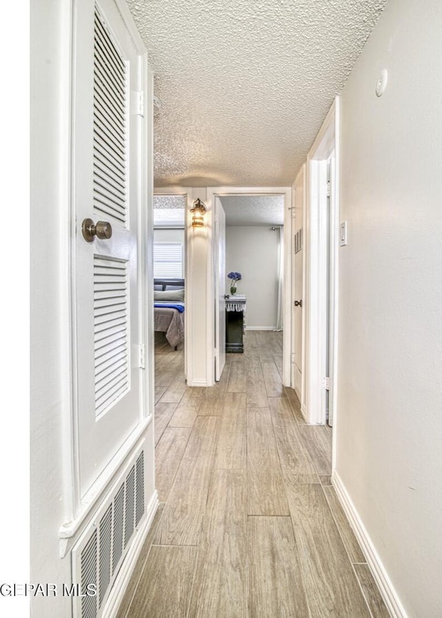 hall featuring visible vents, baseboards, a textured ceiling, and wood finished floors