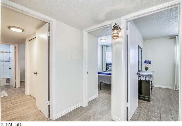 hall with baseboards, a textured ceiling, and light wood-style floors