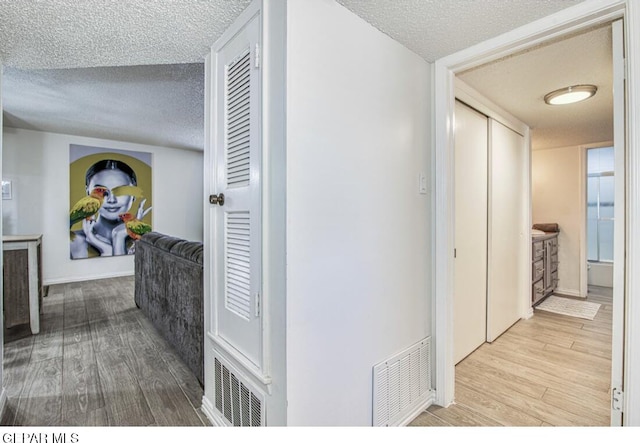 hall with visible vents, a textured ceiling, and wood finished floors