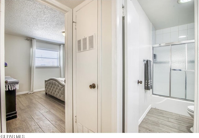 bathroom featuring baseboards, toilet, wood finished floors, enclosed tub / shower combo, and a textured ceiling