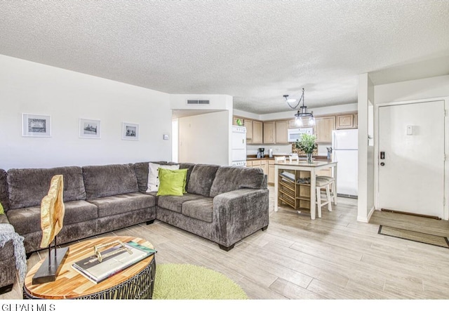 living area featuring light wood-type flooring, visible vents, and a textured ceiling