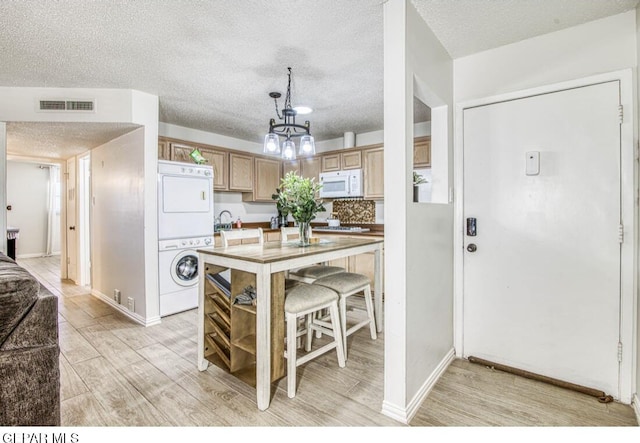 kitchen with white microwave, stacked washer and clothes dryer, an inviting chandelier, light wood-style floors, and a textured ceiling