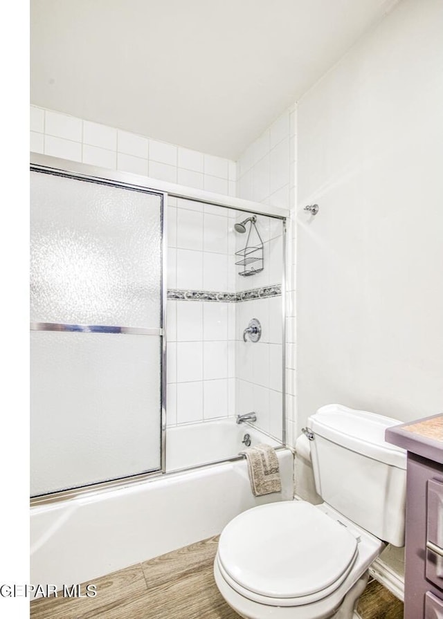 bathroom with combined bath / shower with glass door, toilet, wood finished floors, and vanity