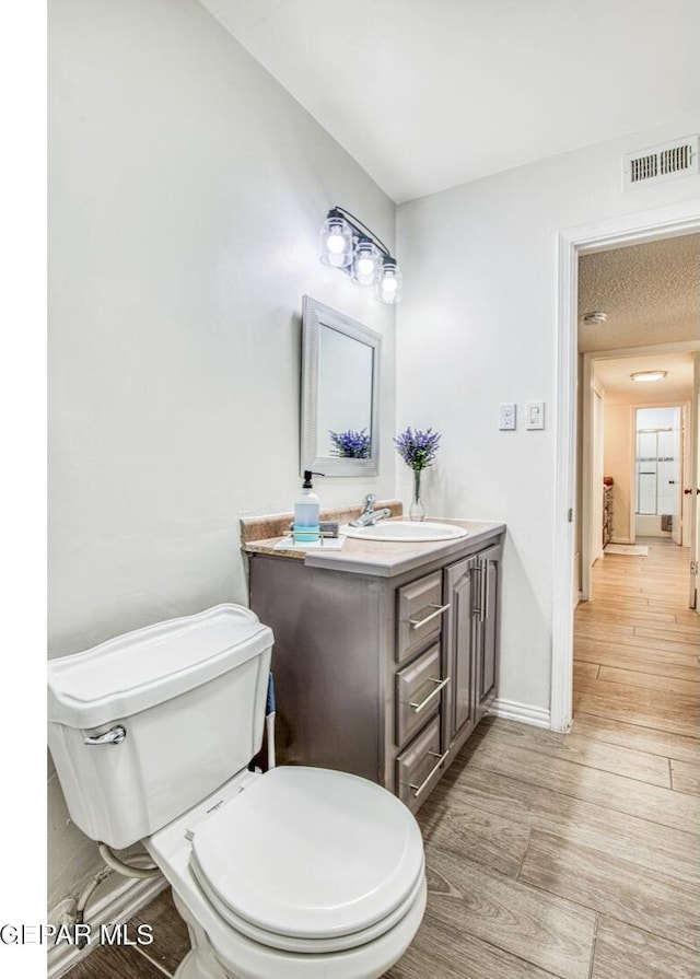 bathroom featuring vanity, wood finished floors, visible vents, baseboards, and toilet