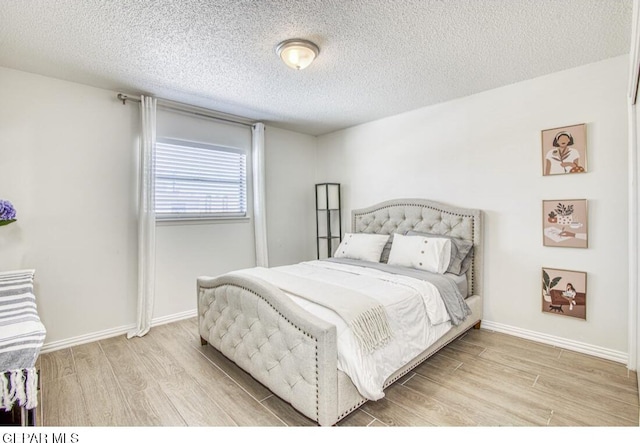 bedroom featuring a textured ceiling, baseboards, and wood finished floors