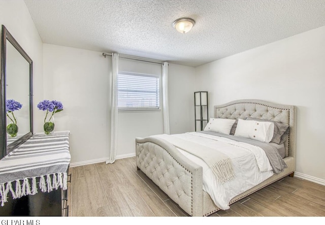 bedroom featuring baseboards, a textured ceiling, and wood finished floors