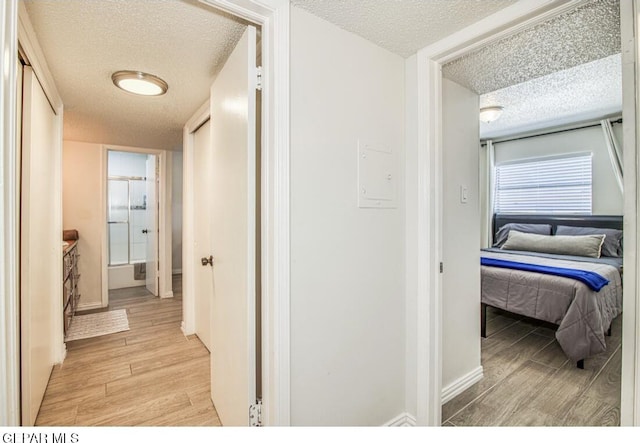 hall featuring light wood finished floors, a textured ceiling, and baseboards