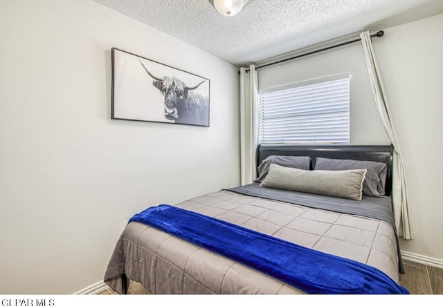 bedroom featuring wood finished floors, baseboards, and a textured ceiling