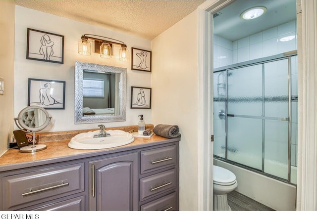 full bathroom with combined bath / shower with glass door, a textured ceiling, vanity, and toilet