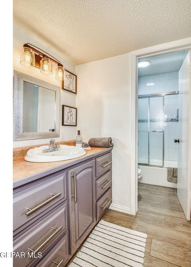 bathroom featuring toilet, a textured ceiling, wood finished floors, shower / bath combination with glass door, and vanity