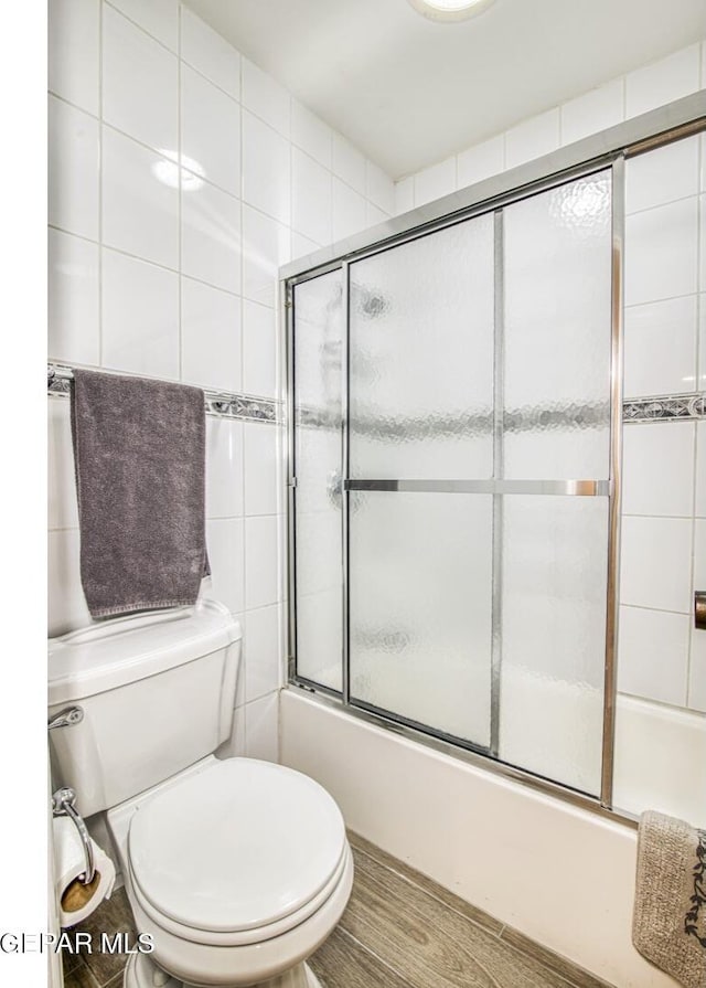 bathroom featuring enclosed tub / shower combo, toilet, and wood finished floors