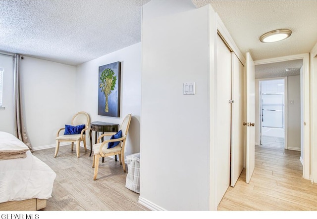 bedroom featuring light wood-type flooring, baseboards, and a textured ceiling