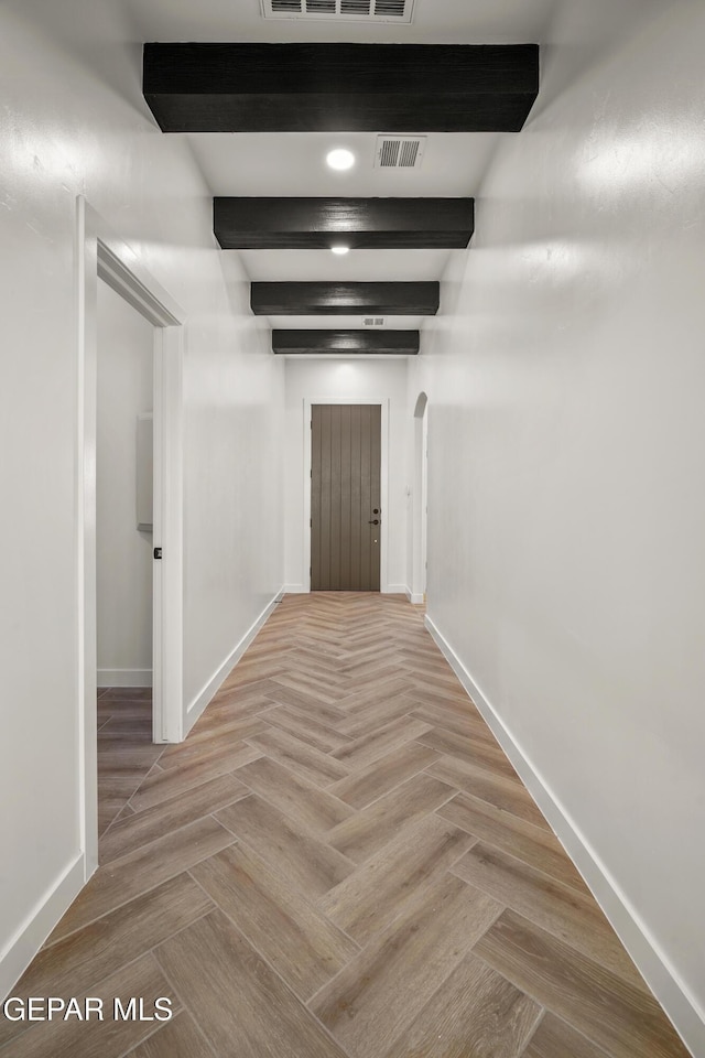 hallway with beam ceiling, baseboards, visible vents, and arched walkways