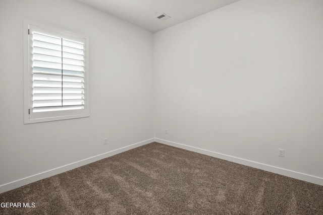 spare room featuring visible vents, baseboards, and dark colored carpet