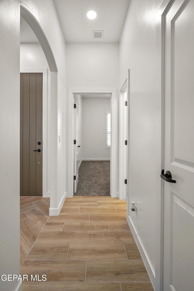 hallway with visible vents, arched walkways, baseboards, and wood tiled floor