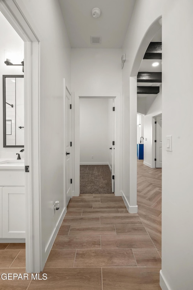 hallway with visible vents, a sink, arched walkways, baseboards, and wood tiled floor