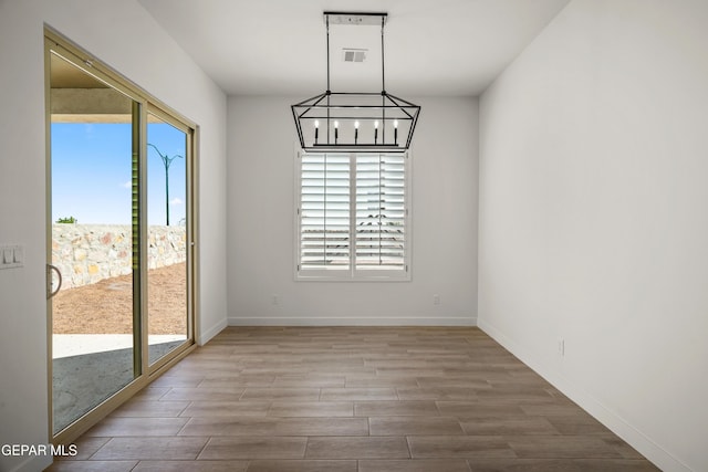 unfurnished dining area featuring a notable chandelier, wood finished floors, visible vents, and baseboards