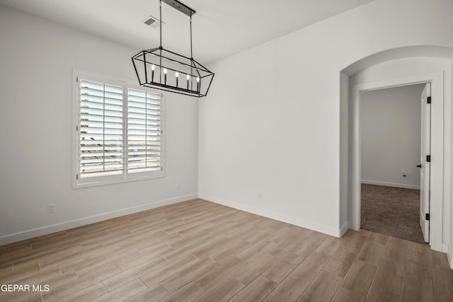 unfurnished dining area with visible vents, a notable chandelier, arched walkways, light wood-style floors, and baseboards