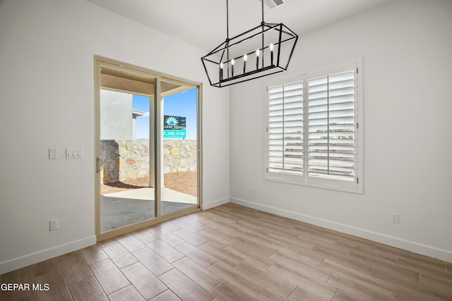 unfurnished dining area featuring an inviting chandelier, wood finished floors, baseboards, and visible vents