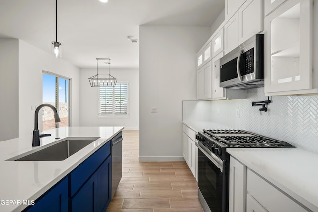 kitchen featuring blue cabinets, a sink, stainless steel appliances, white cabinets, and decorative backsplash