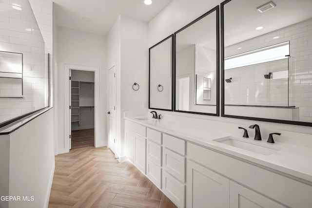 bathroom with double vanity, walk in shower, visible vents, and a sink