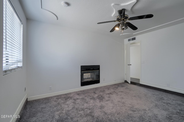 unfurnished living room with visible vents, baseboards, carpet flooring, a glass covered fireplace, and a ceiling fan