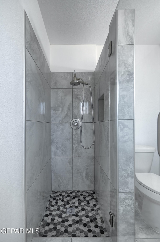 bathroom with toilet, a shower stall, and a textured ceiling