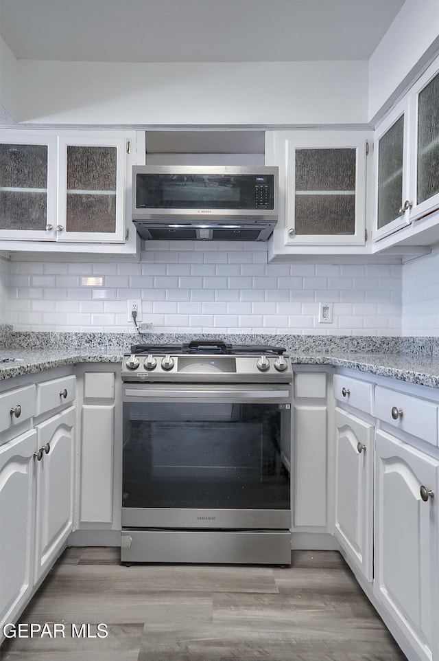 kitchen featuring tasteful backsplash, light wood finished floors, glass insert cabinets, extractor fan, and stainless steel range with gas stovetop