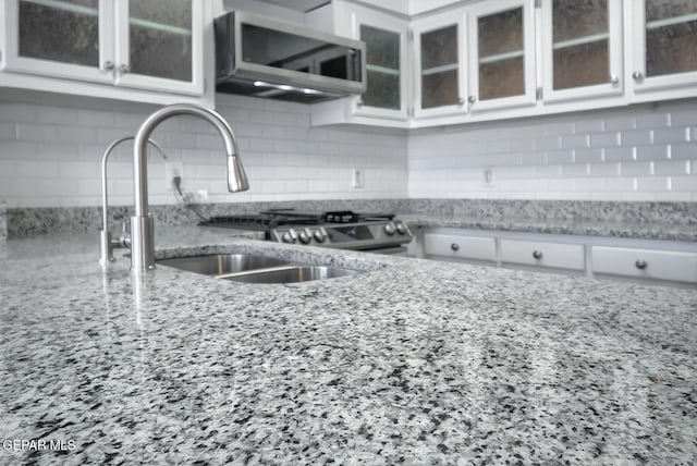 kitchen featuring a sink, stainless steel microwave, backsplash, and white cabinetry