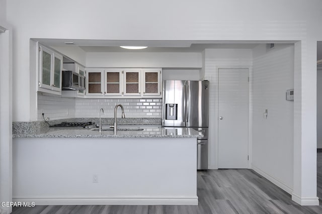 kitchen featuring a sink, appliances with stainless steel finishes, a peninsula, glass insert cabinets, and light stone countertops